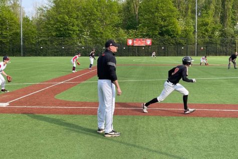 Matthew Furst (23) creeps down the third baseline as Head Coach Terry Gladis looks toward home plate. The baseball teams won three games against  the International School of Brussels and the American School of The Hague April 30.