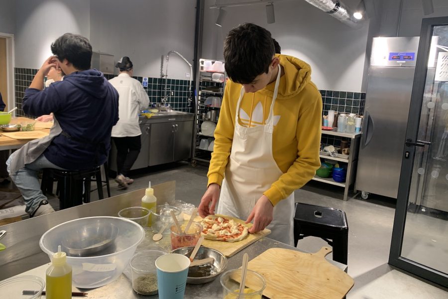 Ethan Rhodes (’25) adds toppings to his pizza as part of the “Courage to Cook” pizza course at Bread Ahead bakery Jan. 26. Students in the group cooked a range of personalized pizzas in preparation for their March trip.